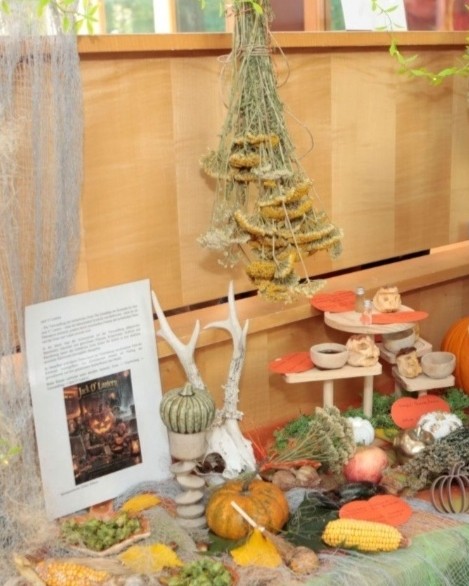Halloween-asztaldekoráció fehér aganccsal, narancs gyertyával, dísz tökökkel, apró söprűkkel és a Jack O' Lantern feliratú ismertetővel
